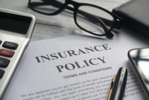 A paper copy of an insurance policy on a desk with a calculator, glasses, pen and smart phone around it.