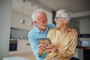 Two happy seniors embracing while looking at a framed photo.